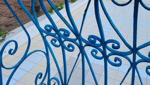 Ein blaues Metallgitter mit aufwendigen Verzierungen, ein mit Fliesen belegter Weg und Palmen im Hintergrund.