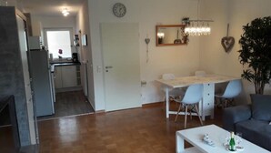 A modern living room with a dining area, a kitchen in the background, and a large potted plant.