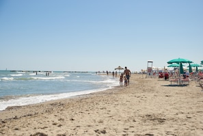 Una spiaggia con persone che passeggiano sulla riva, ombrelloni e lettini.