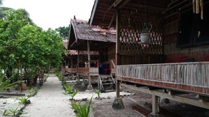 A traditional wooden house with a thatched roof, surrounded by lush greenery and a sandy path. - marine homestay (Pulau Fam)