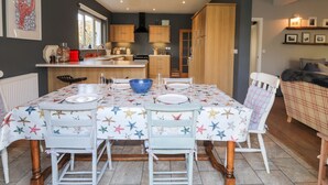 Zona pranzo con tavolo apparecchiato per quattro persone, cucina sullo sfondo e zona living con divano e televisore.