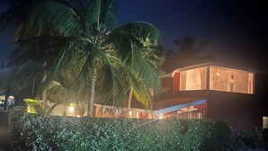 A modern building with a flat roof and large windows, surrounded by lush greenery and palm trees. - Dream villa KEUR BONHEUR in Saly: 3 suites, private pool, 100m from the beach (Saly)