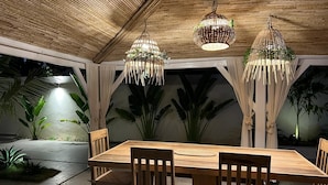 A wooden dining table with chairs, surrounded by large potted plants and a bamboo ceiling. - Dream villa KEUR BONHEUR in Saly: 3 suites, private pool, 100m from the beach (Saly)