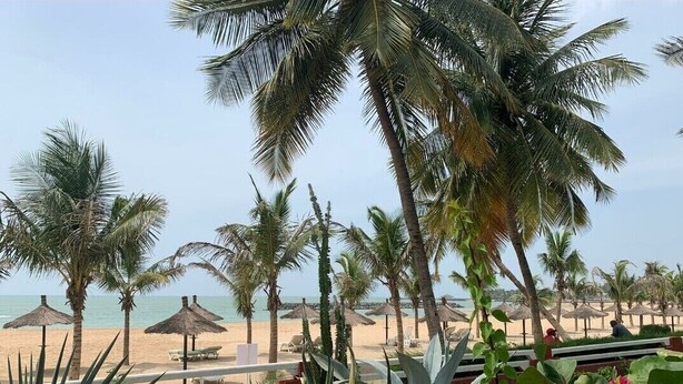 A beachside resort with palm trees, beach umbrellas, and lounge chairs. - Dream villa KEUR BONHEUR in Saly: 3 suites, private pool, 100m from the beach (Saly)