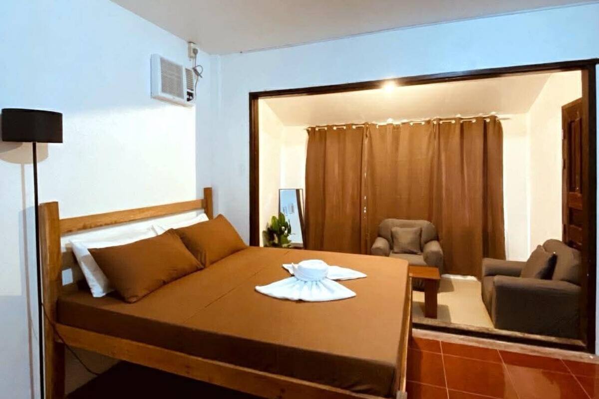 A single bed with a wooden frame, a bedside table, a lamp, and a window with curtains.