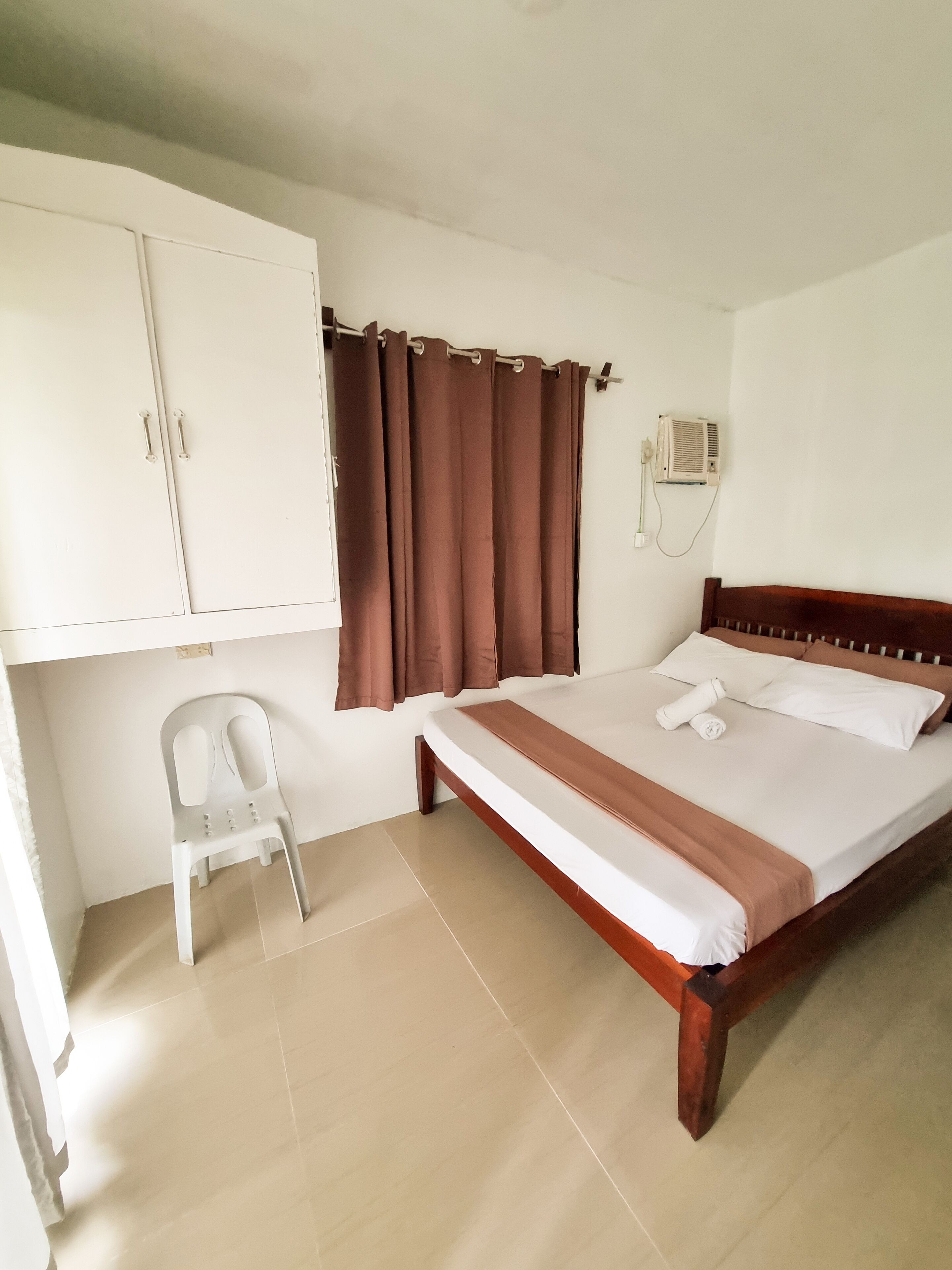 Quarto com cama, uma cadeira, guarda-roupa e cortina.