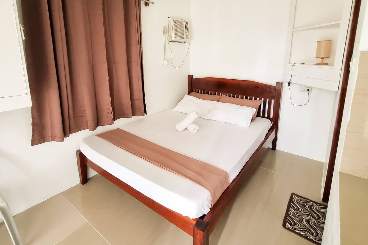 A neatly made bed with a wooden headboard, a bedside table, and a wall-mounted air conditioning unit.