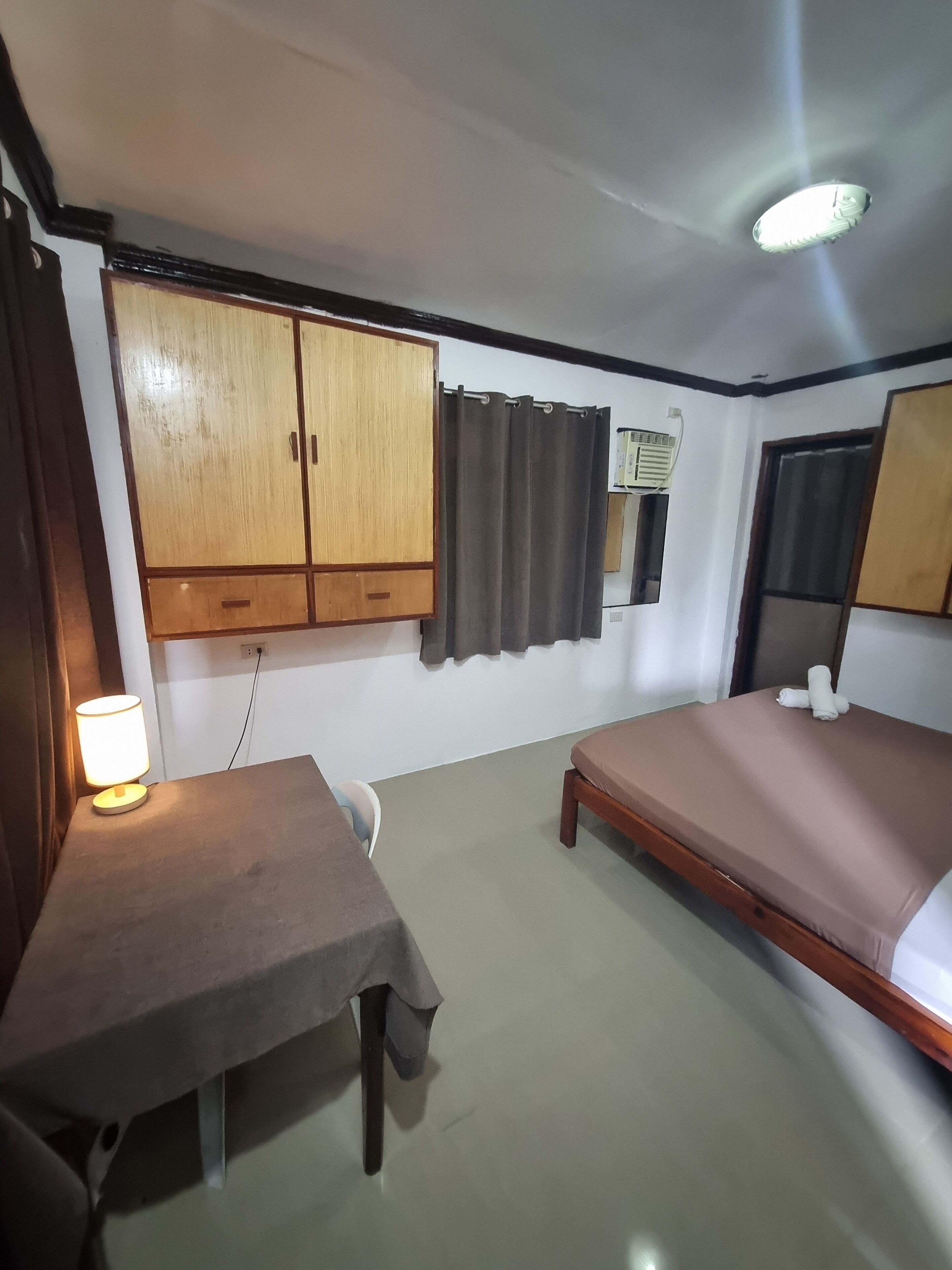 A room with a bed, a desk, a lamp, a wardrobe, and an air conditioning unit.