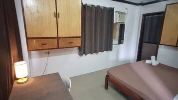 A room with a bed, a desk, a lamp, a wardrobe, and an air conditioning unit.