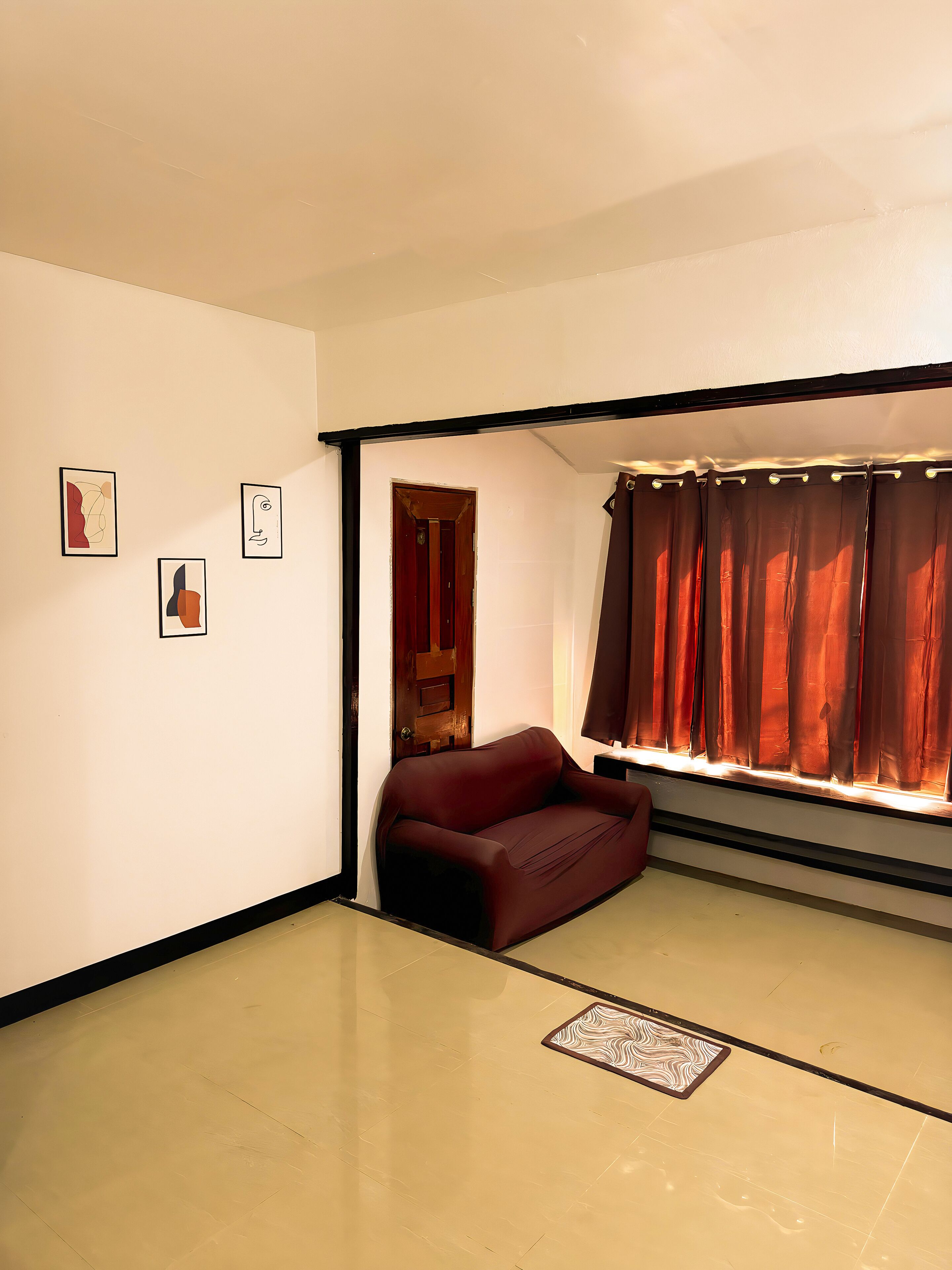Um quarto com um sofá de couro marrom, uma porta de madeira e uma janela com cortinas marrons.