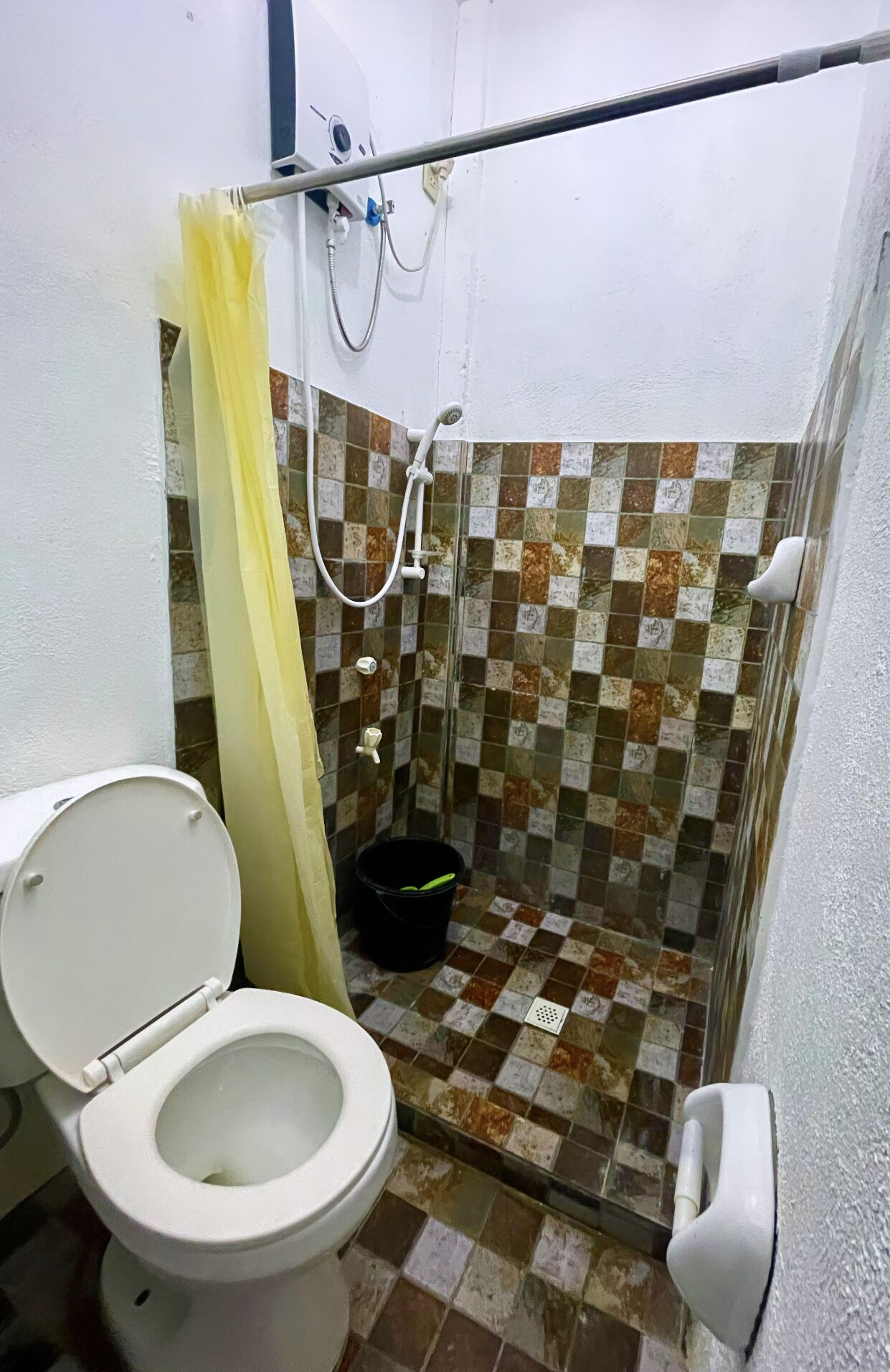A small bathroom with a toilet, a shower, and a tiled shower wall.