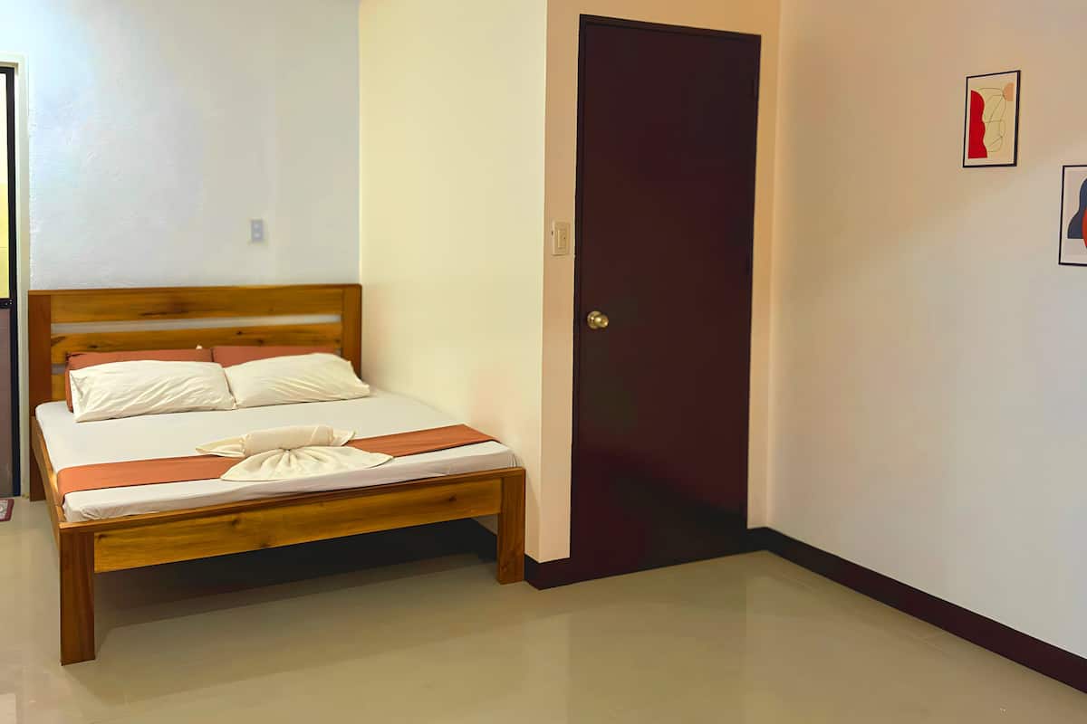 A bedroom with a bed, a door, and a wall with two framed pictures.
