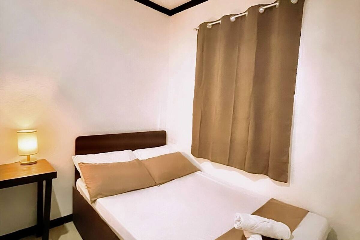 A neatly made bed with a headboard, a bedside table with a lamp, and a window with curtains.