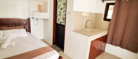 A hotel room with a bed, a small bathroom, and a window with a curtain.