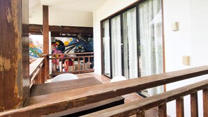 A wooden staircase leading to a balcony with a view of a colorful mural and a large window with curtains. - Flo Island Home (General Luna)