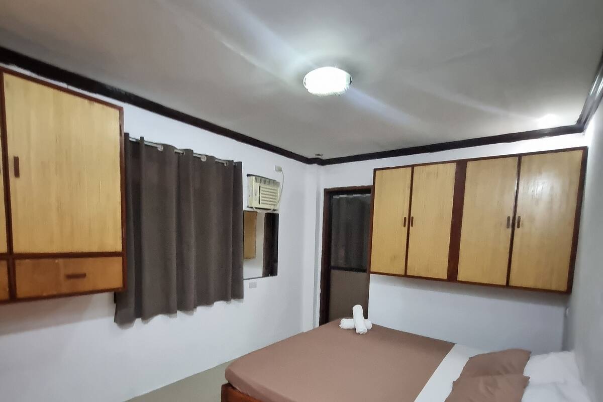 A bedroom with a single bed, wooden wardrobes, a desk, and a window with curtains.