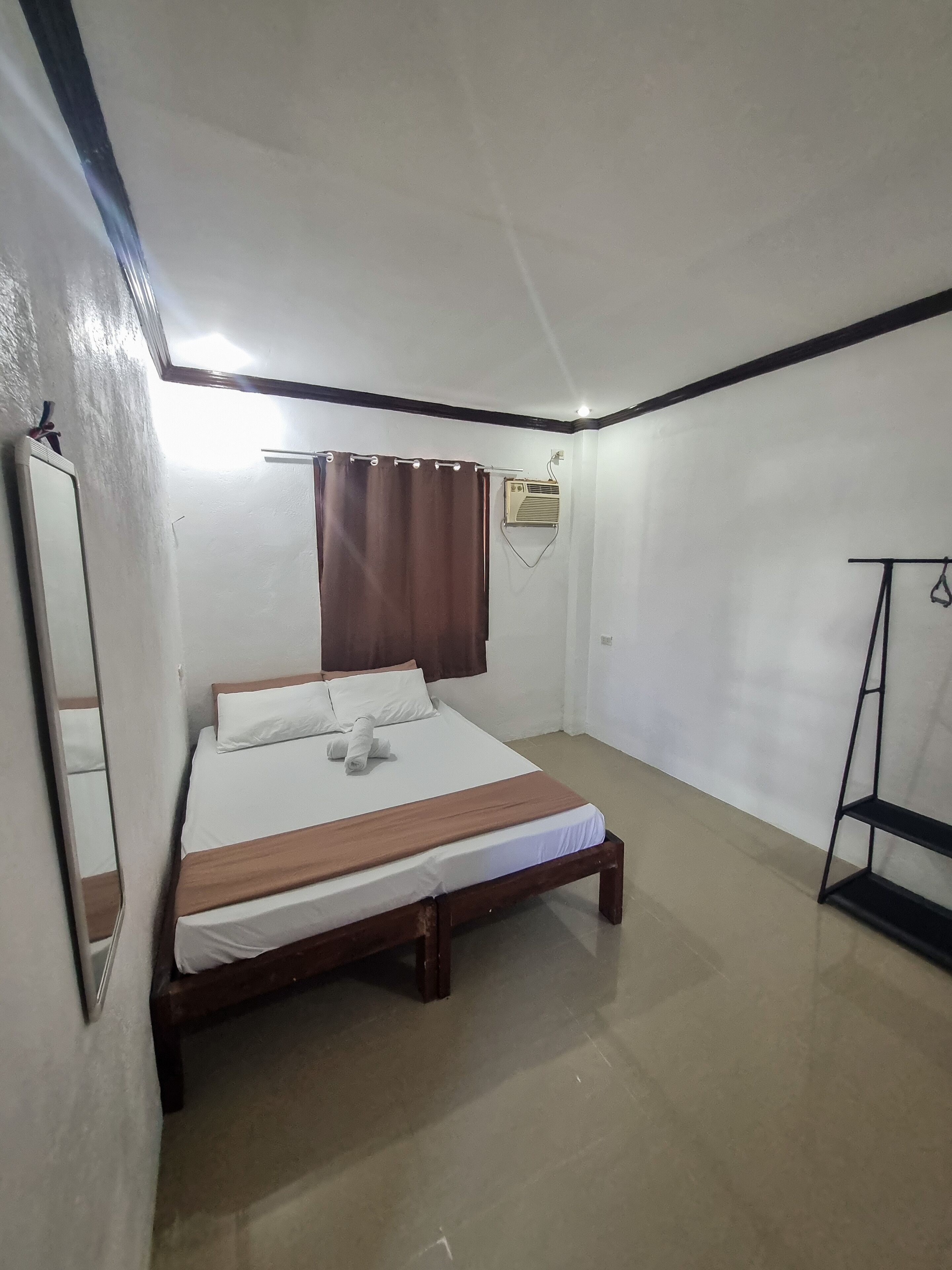 A bedroom with a bed, a window with curtains, an air conditioning unit, and a black metal shelf.