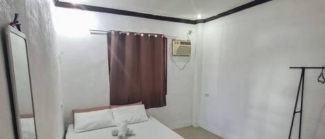 A bedroom with a bed, a window with curtains, an air conditioning unit, and a black metal shelf.