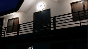 A modern building with a prominent 'flo' sign on the facade, a balcony with a railing, and a dark sky indicating nighttime. - Flo Island Home (General Luna)