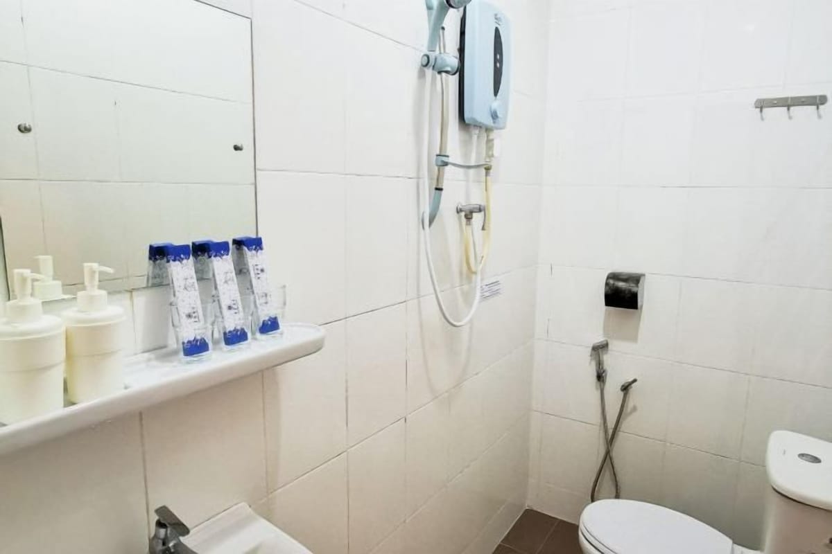 Une salle de bain avec un lavabo blanc, un miroir, une douche équipée d’un pommeau de douche amovible et des toilettes.