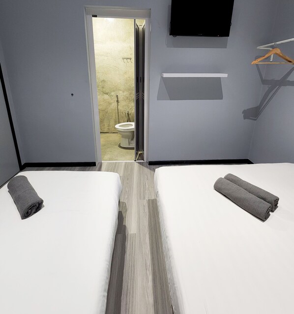 A hotel room with two beds, a bathroom visible through an open door, a mounted TV, and a towel rack.