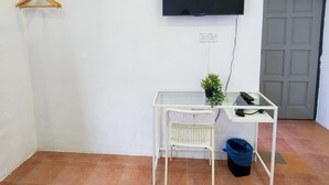 Una habitación con aire acondicionado blanco, televisor montado, una pequeña mesa blanca con una planta y una puerta.