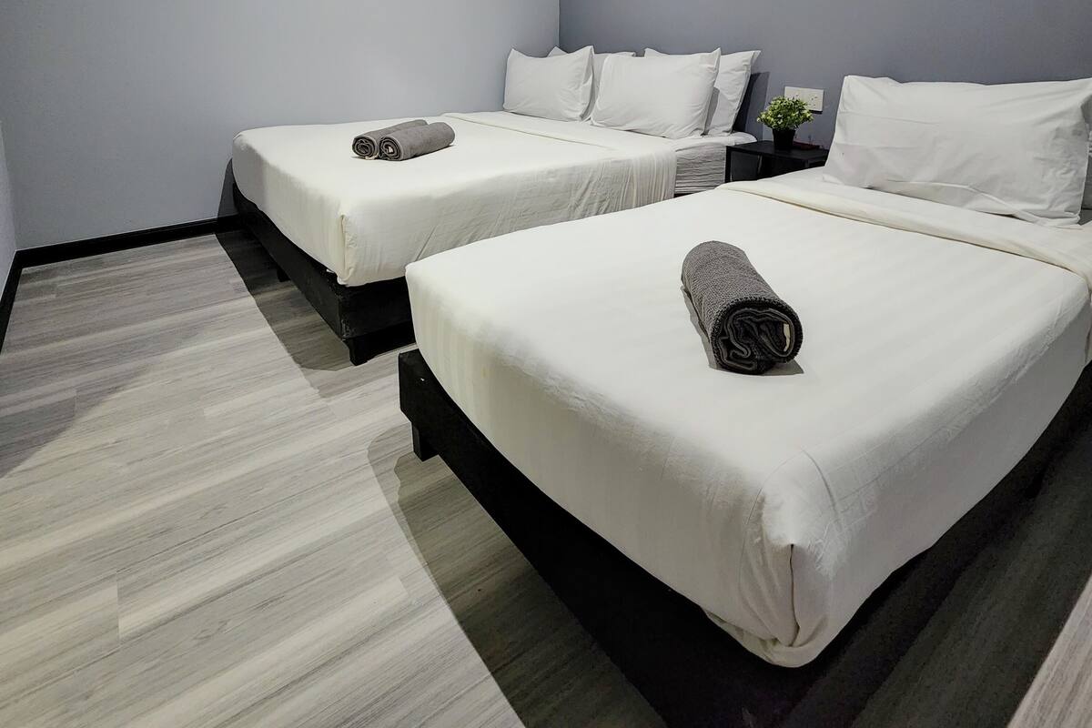 A hotel room with two beds, each with white linens and a rolled towel on the bed. The room has a modern design with a grey and white color scheme.