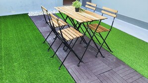 Un área de comedor al aire libre con una mesa y sillas de madera, rodeada de césped artificial y una terraza de madera.