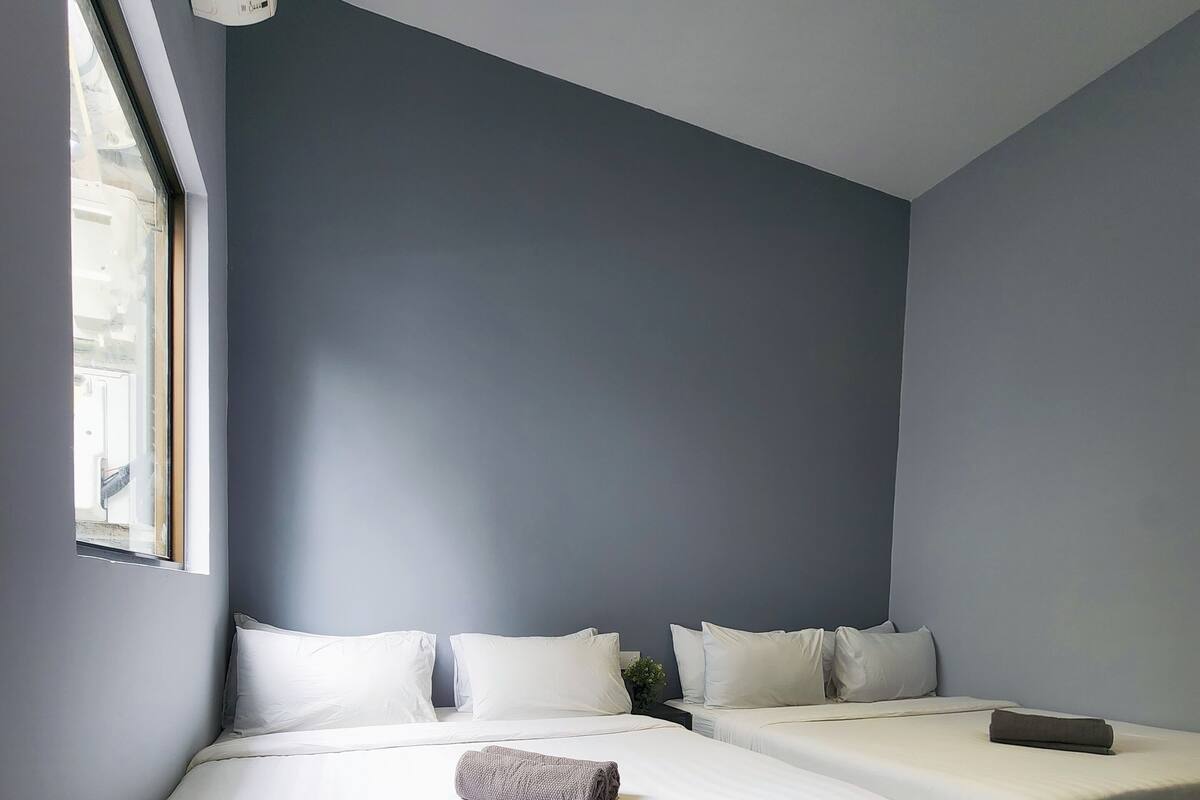 A modern hotel room with two beds, a large window, and a built-in air conditioning unit.