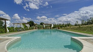 A clear swimming pool with a pergola and lounge chairs.