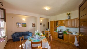 A compact kitchen with wooden cabinets, a dining table set for four, and a blue sofa in the living area. - Tramonto apartment, Charming Farmhouse Private Pool and Private Outside Area (Toscana)