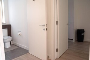 A room with a white door, a toilet, a trash bin, and a wooden floor.