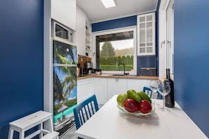 A compact kitchen with white cabinets, a dining table with a bowl of fruit, and a view of the outdoors.