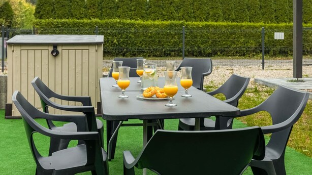 Un área de estar al aire libre con una mesa para dos, rodeada de sillas, y un cobertizo pequeño al fondo.