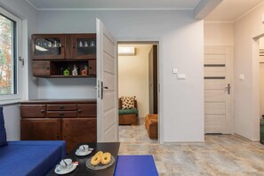 Un espacio habitable compacto con kitchenette, un comedor con mesa para dos, y una pequeña sala de estar con sofá y sillón.