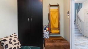 Una habitación con un armario oscuro, un banco, una mesita con una cesta y una toalla amarilla colgada en un perchero de madera.