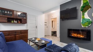 Una sala de estar moderna con un sofá, una mesa de centro, una chimenea, un televisor y un mueble de madera con puertas de cristal.