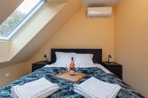 Un dormitorio con cama, mesita de noche, lámpara de noche, ventana y aire acondicionado.