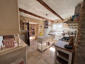 A rustic kitchen with exposed beams, a stone wall, and a view into the dining area.