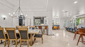 A spacious dining area with a high ceiling, modern chandelier, and a view of the kitchen in the background. - Walk to Beach / Heated Pool / Serenity at its Finest / Hemingway Key / VlLLAS (Fort Lauderdale)