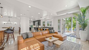 A spacious living area with a large sectional sofa, a dining table with chairs, and a kitchen in the background. - Walk to Beach / Heated Pool / Serenity at its Finest / Hemingway Key / VlLLAS (Fort Lauderdale)