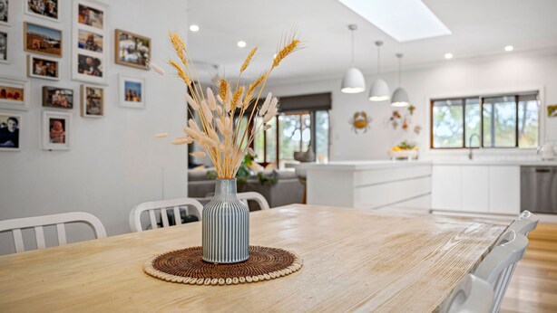 A dining area with a wooden table, a vase with dried wheat stalks, and a wall adorned with framed photographs. - The Homestead on Hopkins (Aireys Inlet)