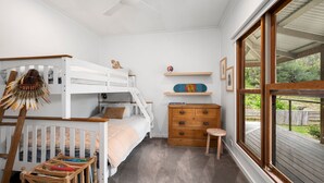 A child's room with bunk beds, a dresser, a small stool, and a window with a view of greenery. - The Homestead on Hopkins (Aireys Inlet)