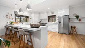 A modern kitchen with a central island, bar stools, a refrigerator, and a large window. - The Homestead on Hopkins (Aireys Inlet)