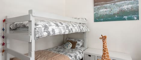 A bunk bed room with a giraffe toy, a beach-themed painting, and a wicker storage unit.