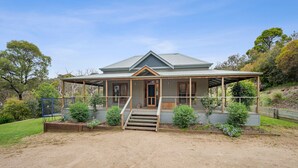 A two-story house with a covered porch, a front door, and a staircase leading to the entrance. - The Homestead on Hopkins (Aireys Inlet)