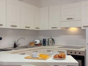 A modern kitchen with white cabinets, a built-in oven, a coffee maker, and breakfast items on the counter.