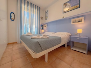 A bedroom with a bed, bedside tables, a nightstand, a window with curtains, and wall art.