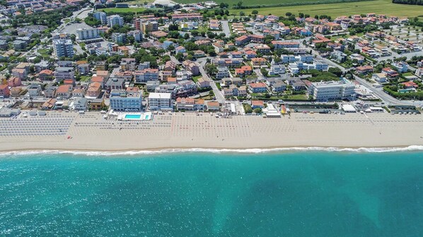 An aerial view of a coastal town with residential buildings, a beach, and a swimming pool.