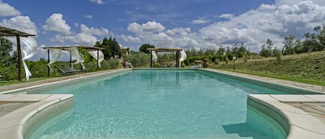 A clear swimming pool with a pergola and lounge chairs.